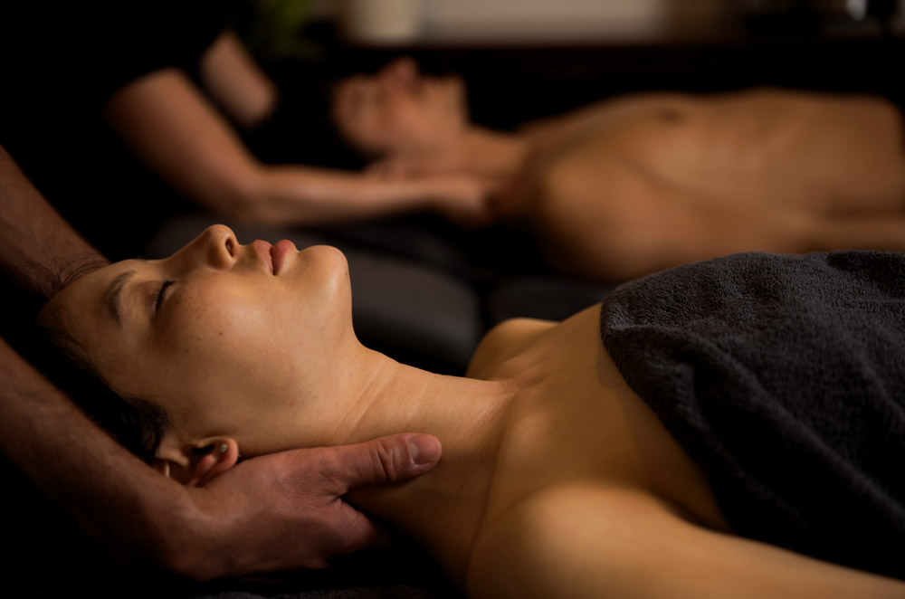 Couple homme femme massage DUO à deux couchés sur le dos. Visages détendus, pénombre, serviettes noires Relaxant