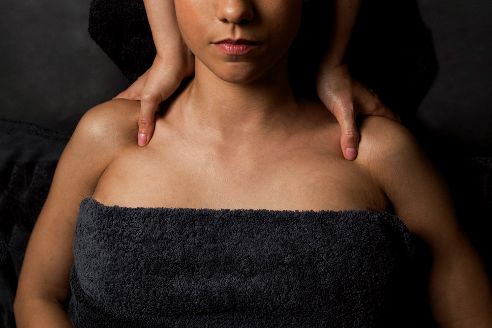 Femme sur le dos reçoit massage relaxant des épaules et du cou. Pénombre, serviette
